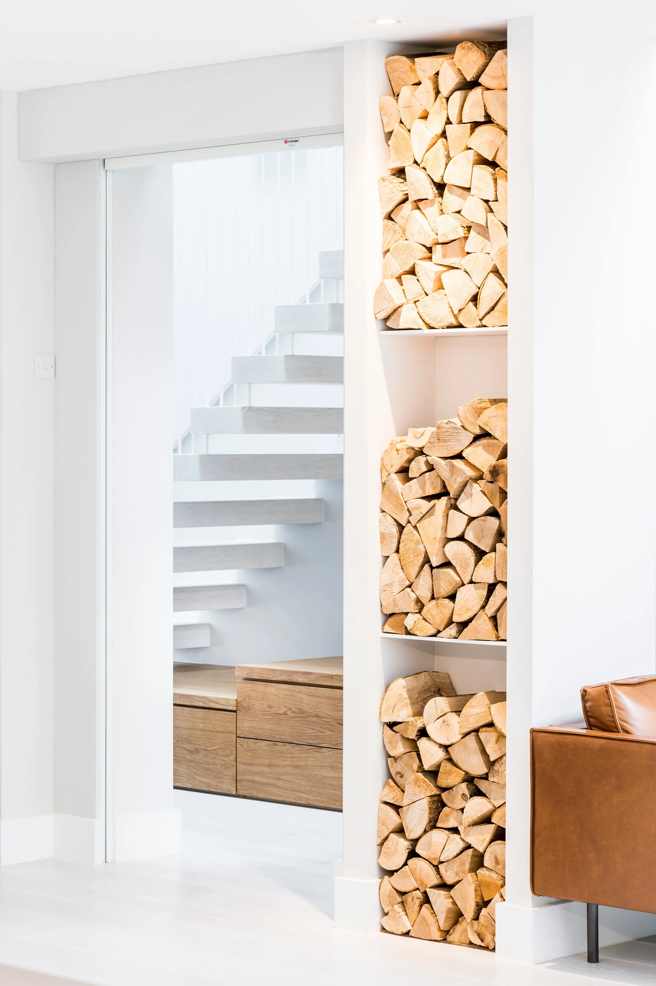 Contemporary interior design featuring a floating oak staircase, bespoke oak storage, illuminated log store and minimalist living space designed by The Pratt Studios.