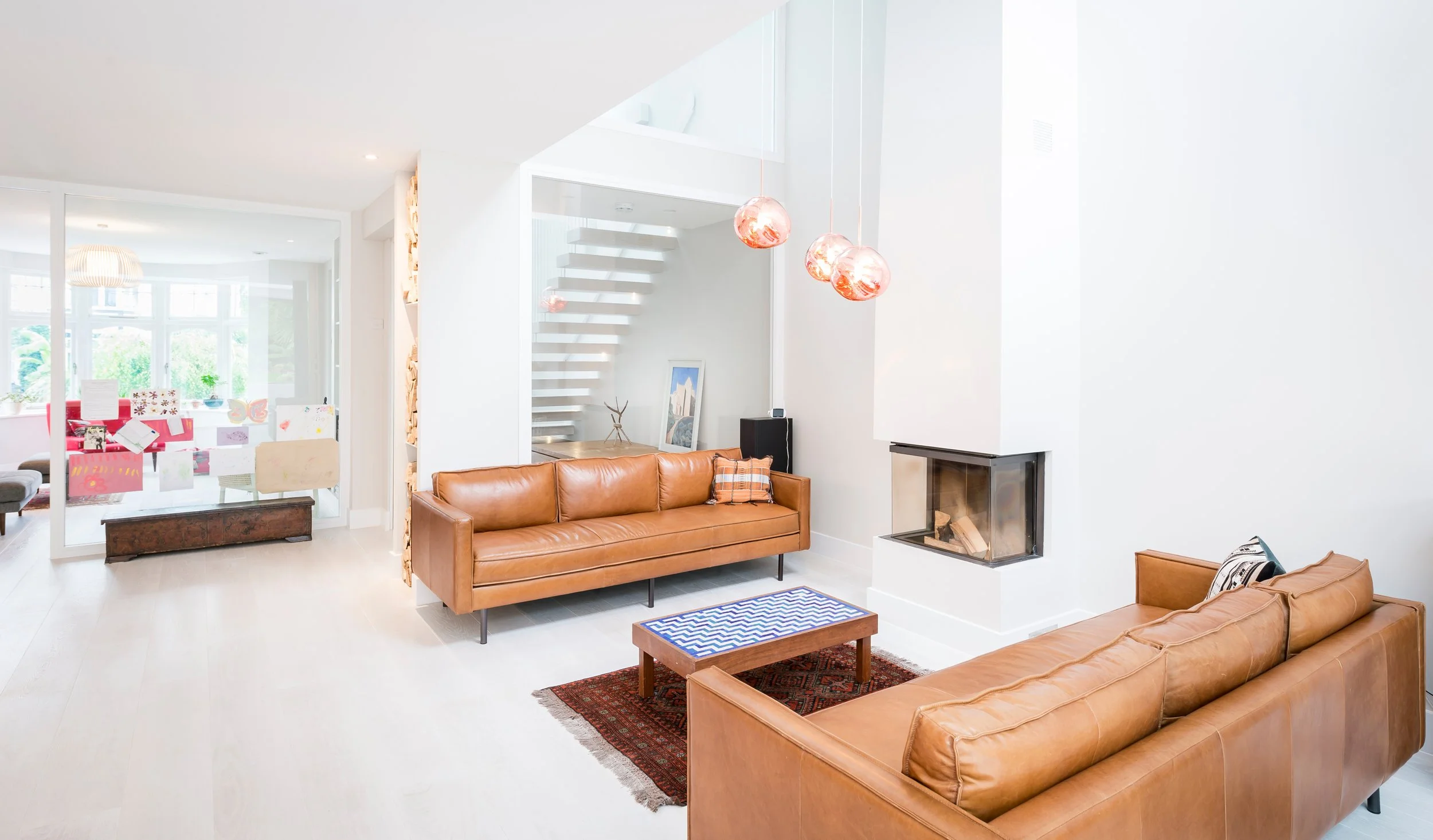 Contemporary open-plan living room with bespoke interior design, floating staircase, feature fireplace and modern furnishings.