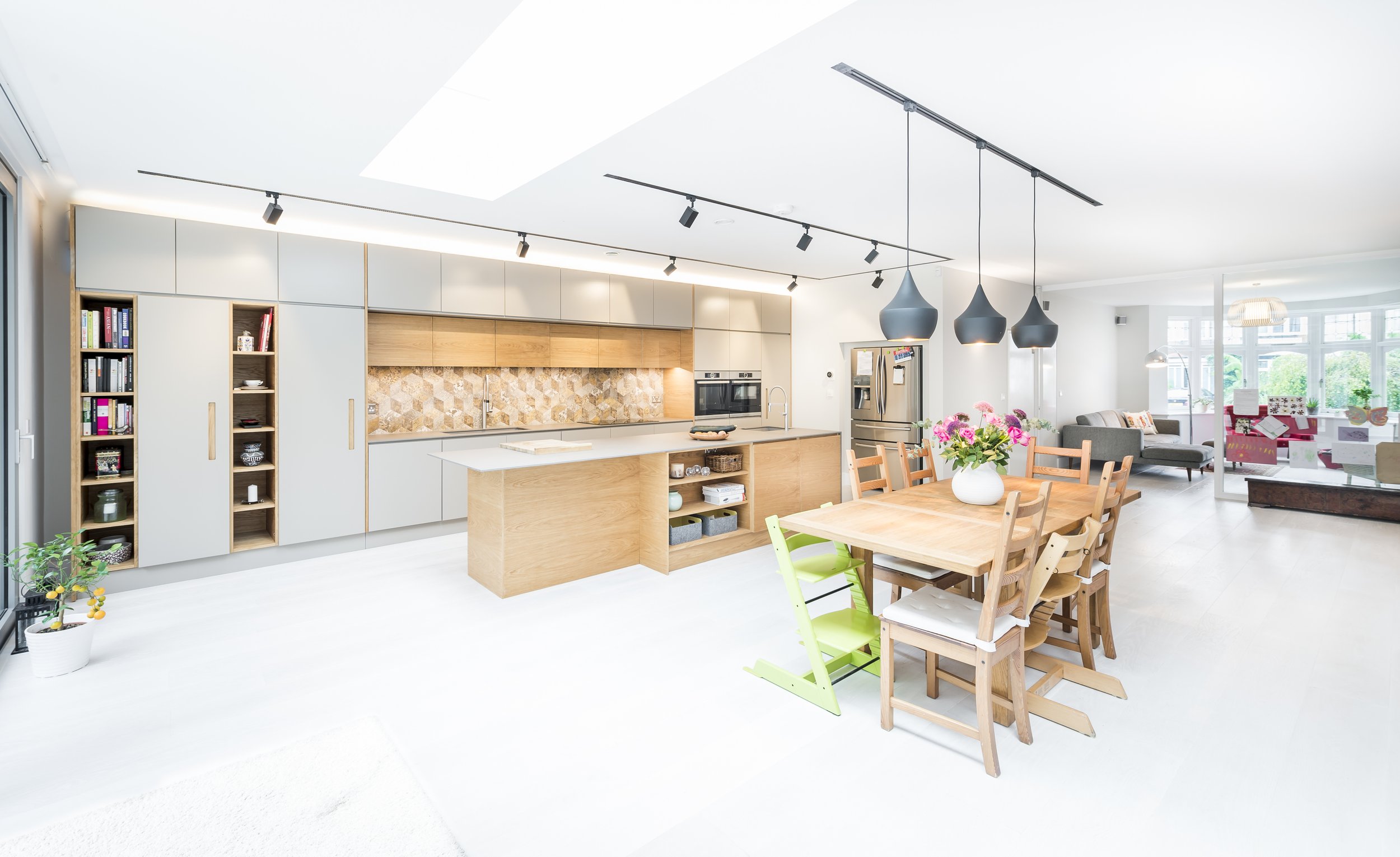 Bright and spacious open-plan kitchen and dining area in a modern family home, featuring minimalist cabinetry, natural wood finishes, pendant lighting, and a casual living space in the background, showcasing contemporary interior design with a homely