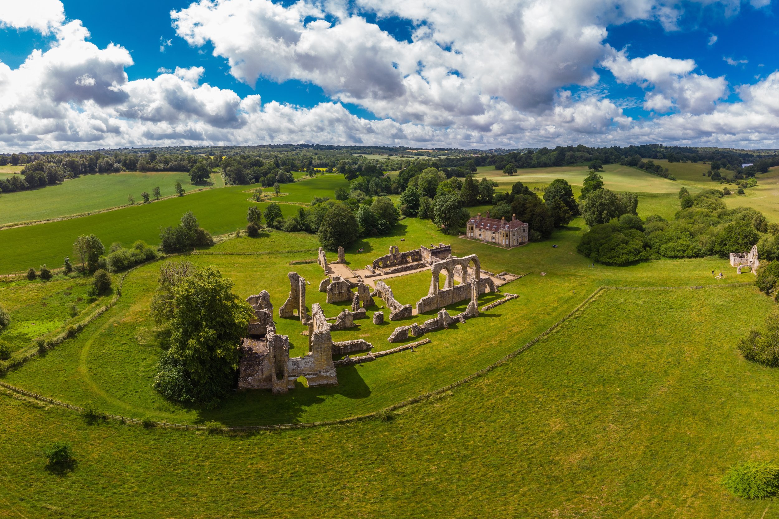 Professional aerial drone photograph of historic abbey ruins surrounded by open countryside and rolling green landscape.