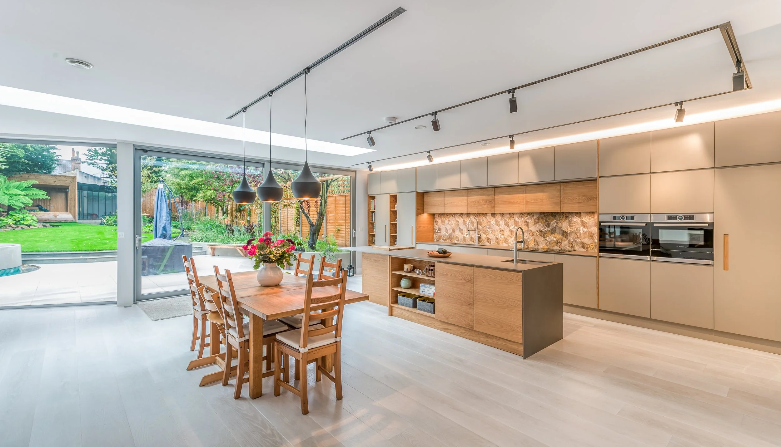 Contemporary open-plan kitchen and dining space featuring bespoke cabinetry, natural materials, statement lighting and seamless indoor-outdoor living.
