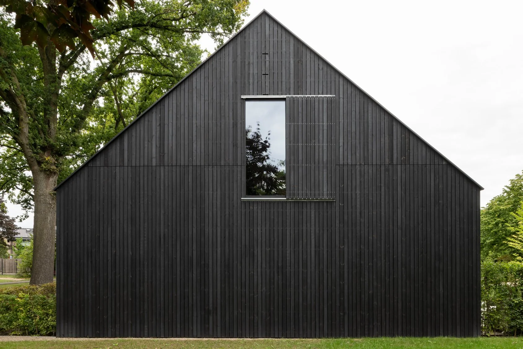 Gable elevation of a contemporary black timber-clad new build commercial building with a central floor-to-ceiling window and minimalist architectural detailing and set amongst beautiful trees.