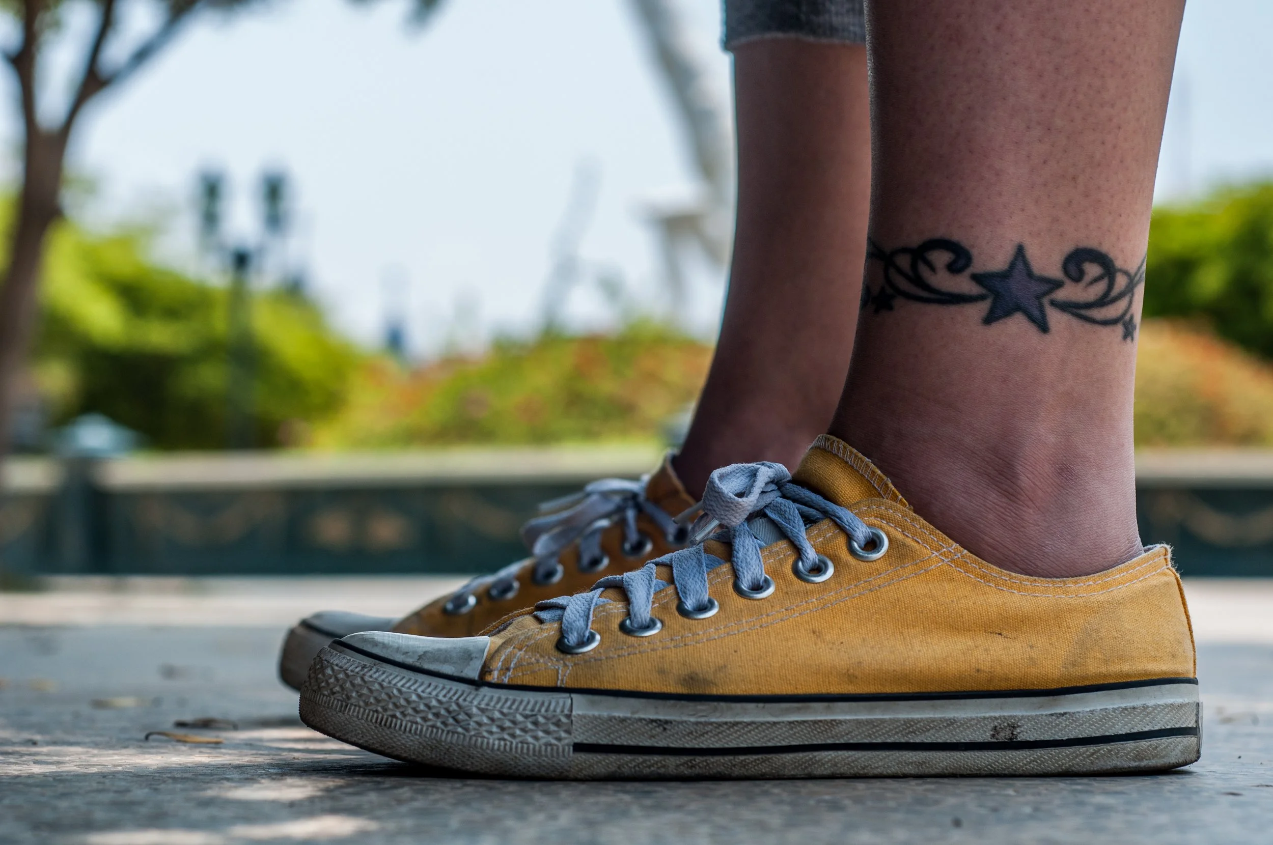 Close-up of yellow low-top Converse sneakers with gray laces, worn outdoors by a person with a star tattoo above the ankle. Archival contextual photo from 2013, not the disputed ad.