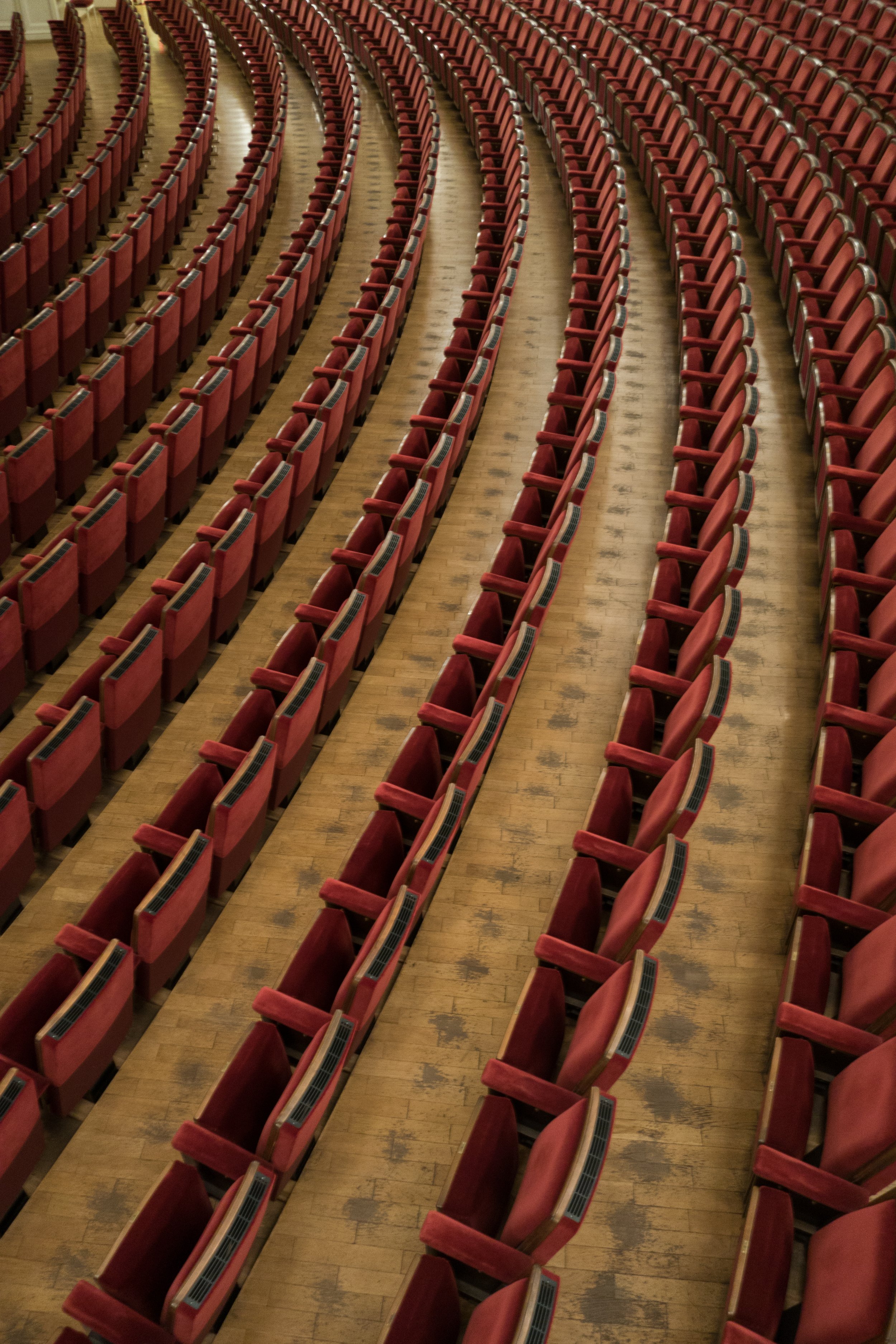 Curved rows of empty red upholstered theatre seats separated by narrow aisles. Archival illustrative photograph in Dresden by Thomas Quine, cropped; not a Broadway venue.