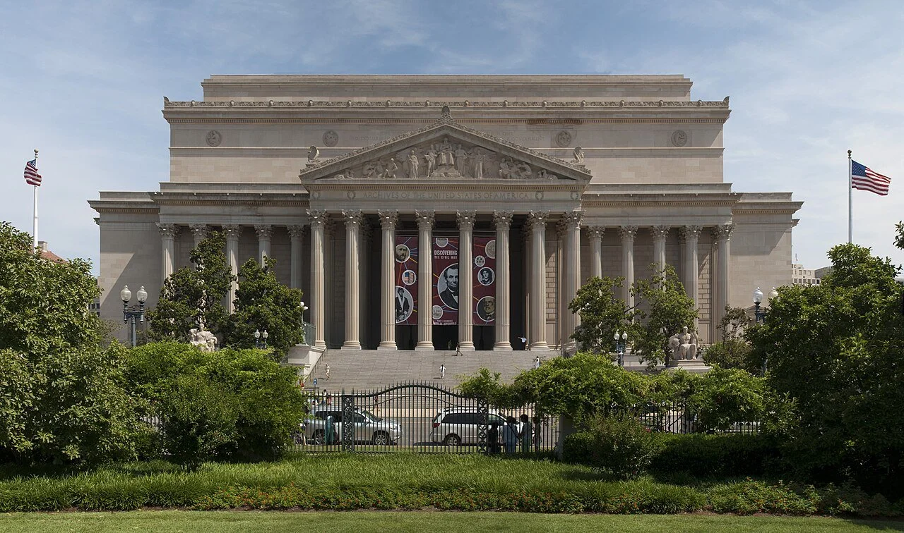 Archival view of the National Archives Building in Washington, D.C., with tall stone columns and broad steps beneath a blue sky. Photograph by David Samuel, May 2010.