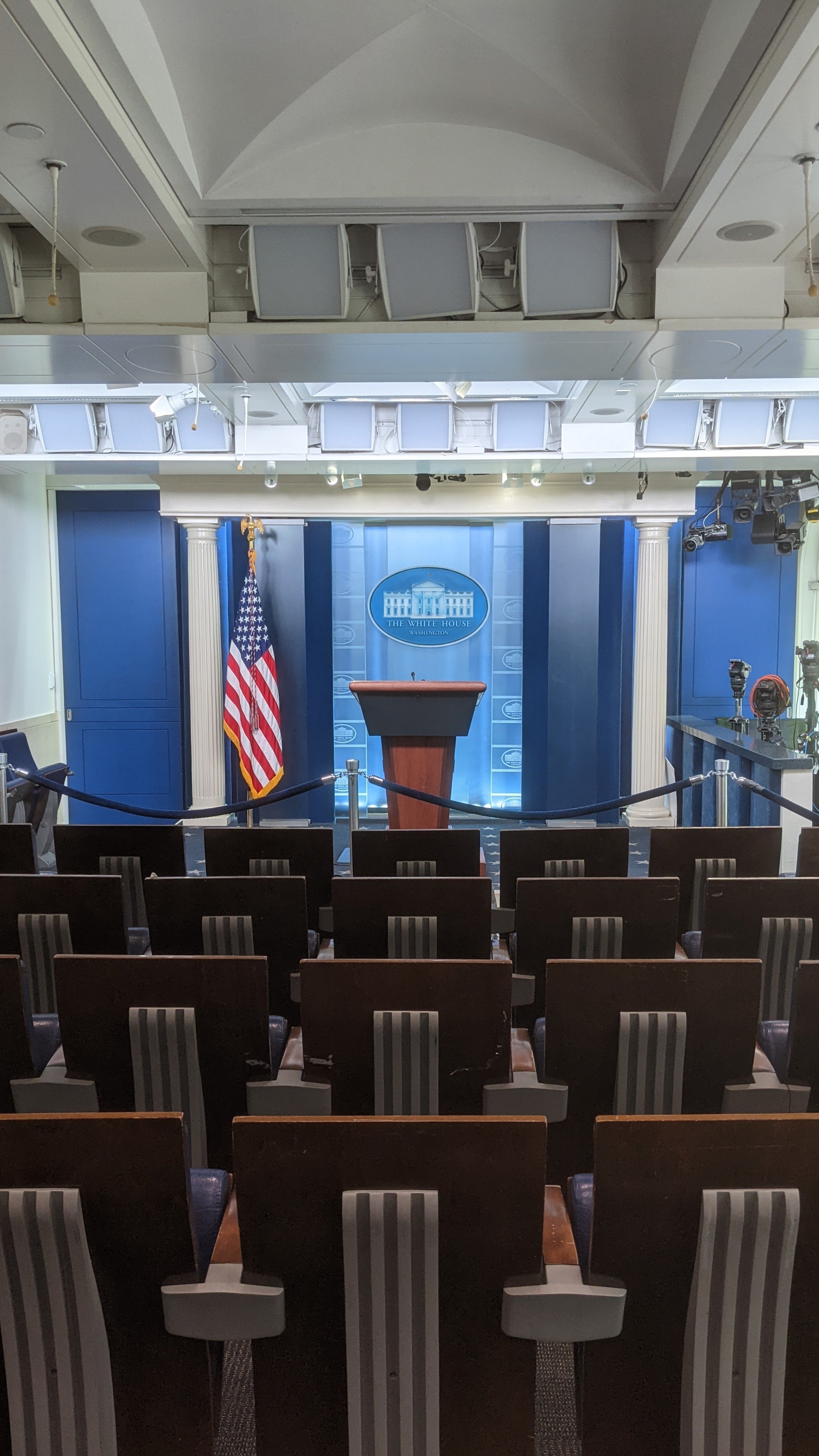 Rows of empty chairs facing the lectern, U.S. flag and blue backdrop in the White House press briefing room. Archival photograph from 2022.