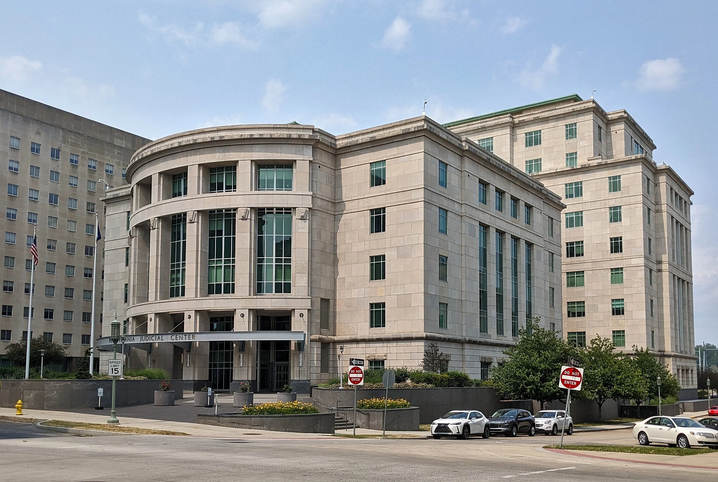 Pennsylvania Judicial Center in Harrisburg, viewed across a street, with its curved stone entrance, tall windows and parked cars. Archival photograph from June 2023.