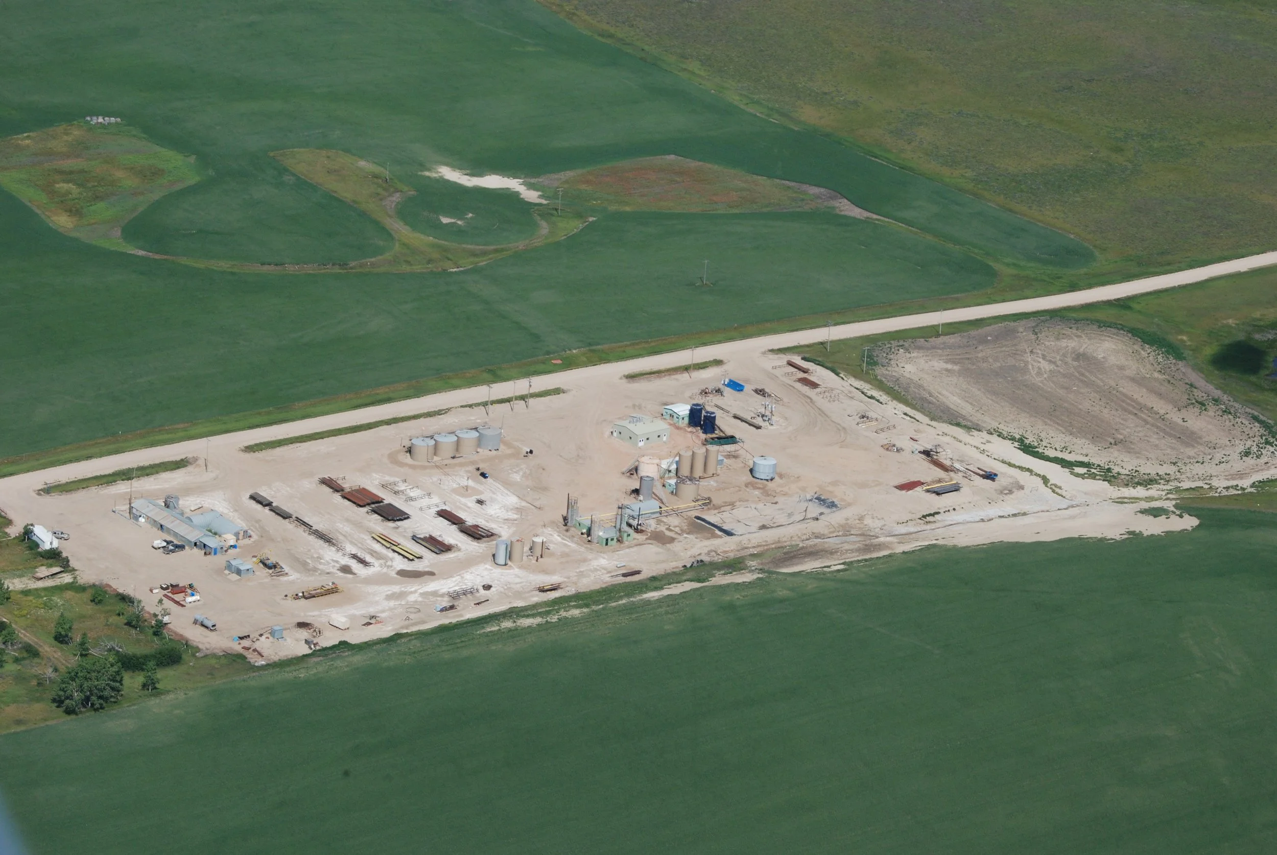 Archival aerial view of oil facilities with cylindrical tanks, equipment and low buildings beside a road and green fields. Photo by Jerry Rodriguez, USFWS, published by USGS in 2009.