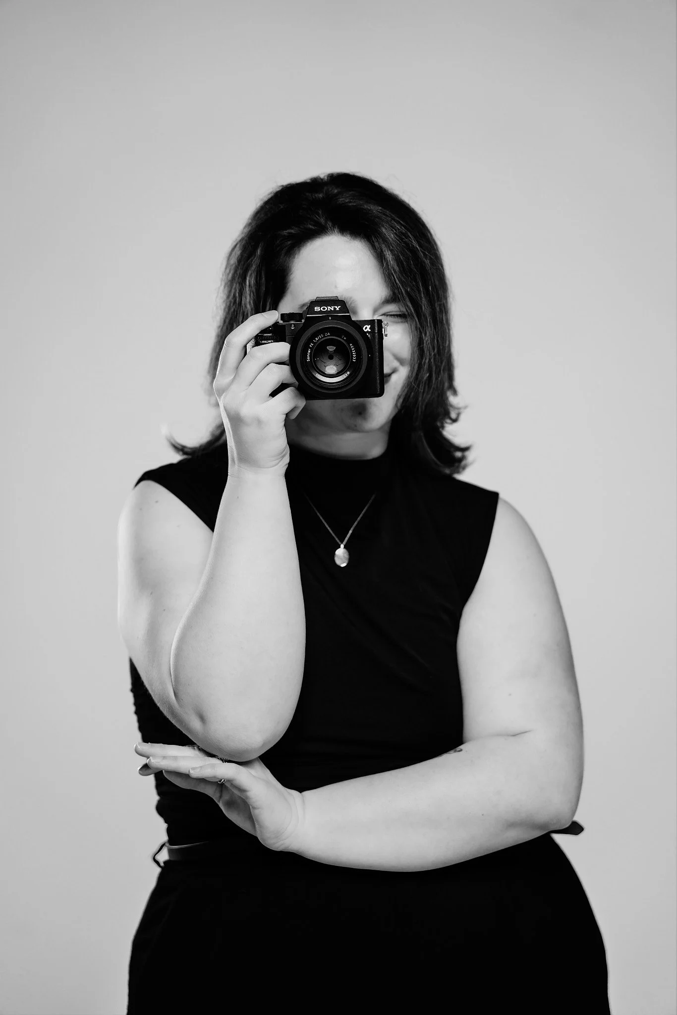 A woman taking a photo with a camera, dressed in black, with shoulder-length dark hair, in a black and white photo.