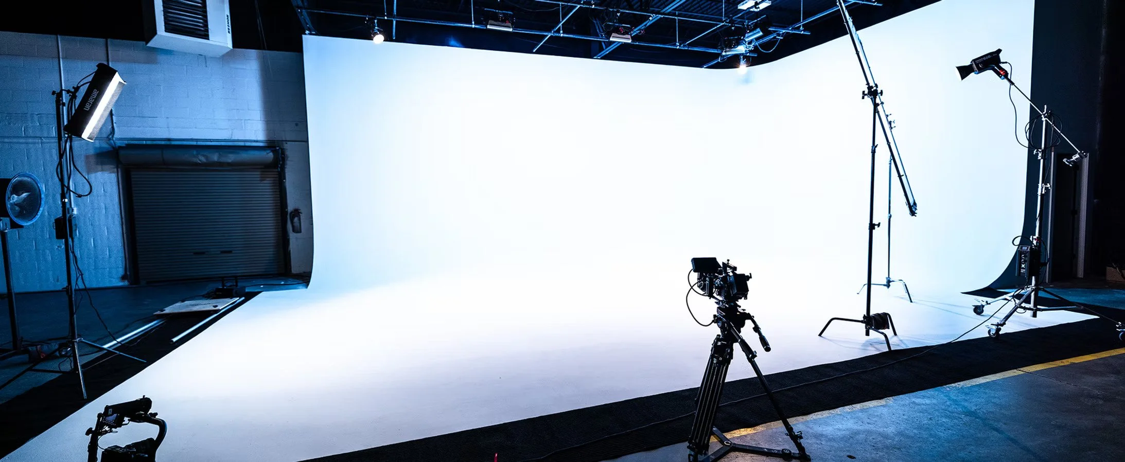 Empty professional photography or video studio with a large white backdrop, cameras, lighting equipment, and stands.