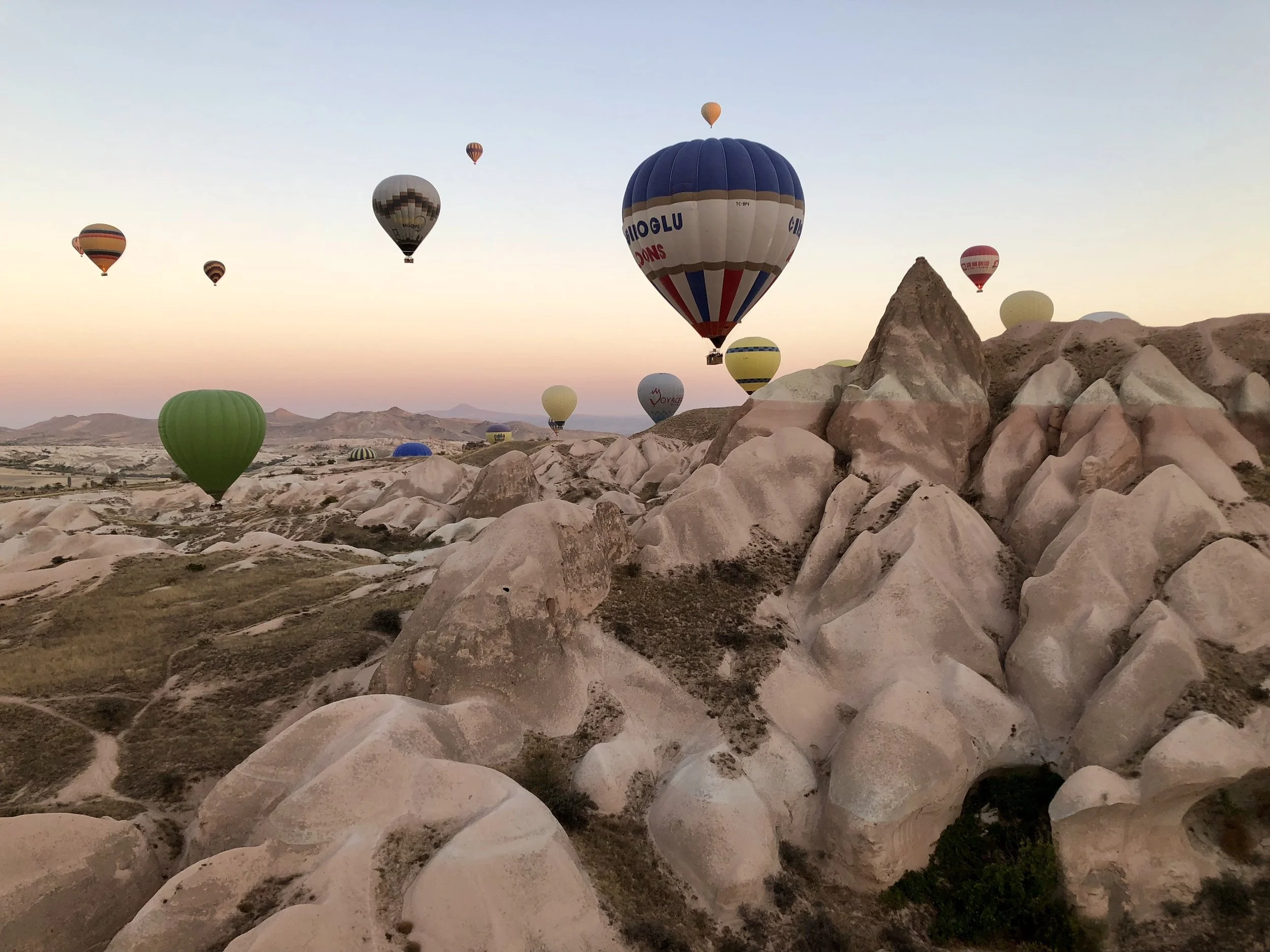 Hot air balloons flying over rocky, desert landscape at sunrise.