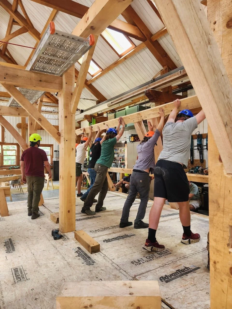 Students lift a timber assembly together during a barn raising.