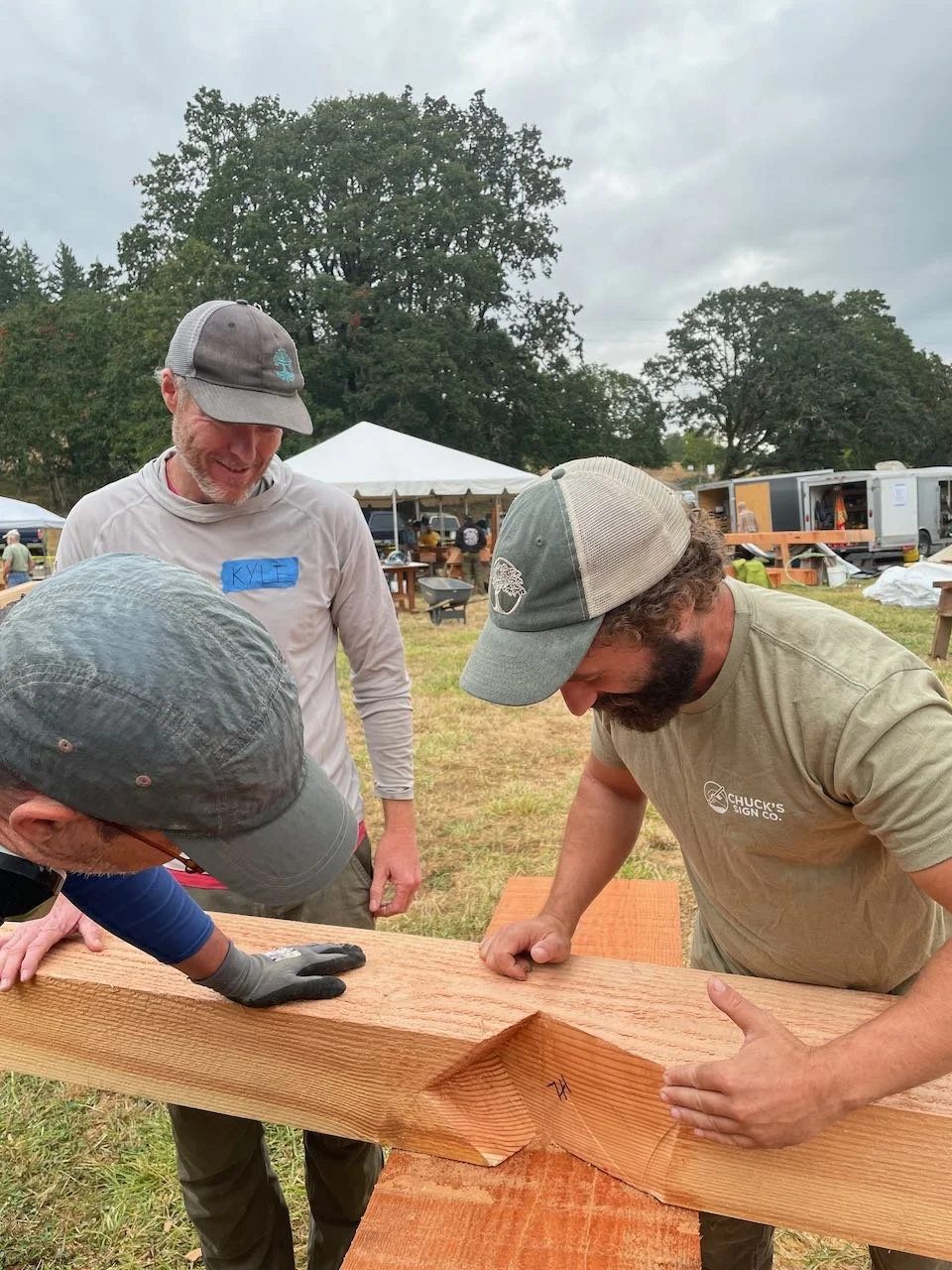 Carpenters talking about hip roof joinery in front of a timber