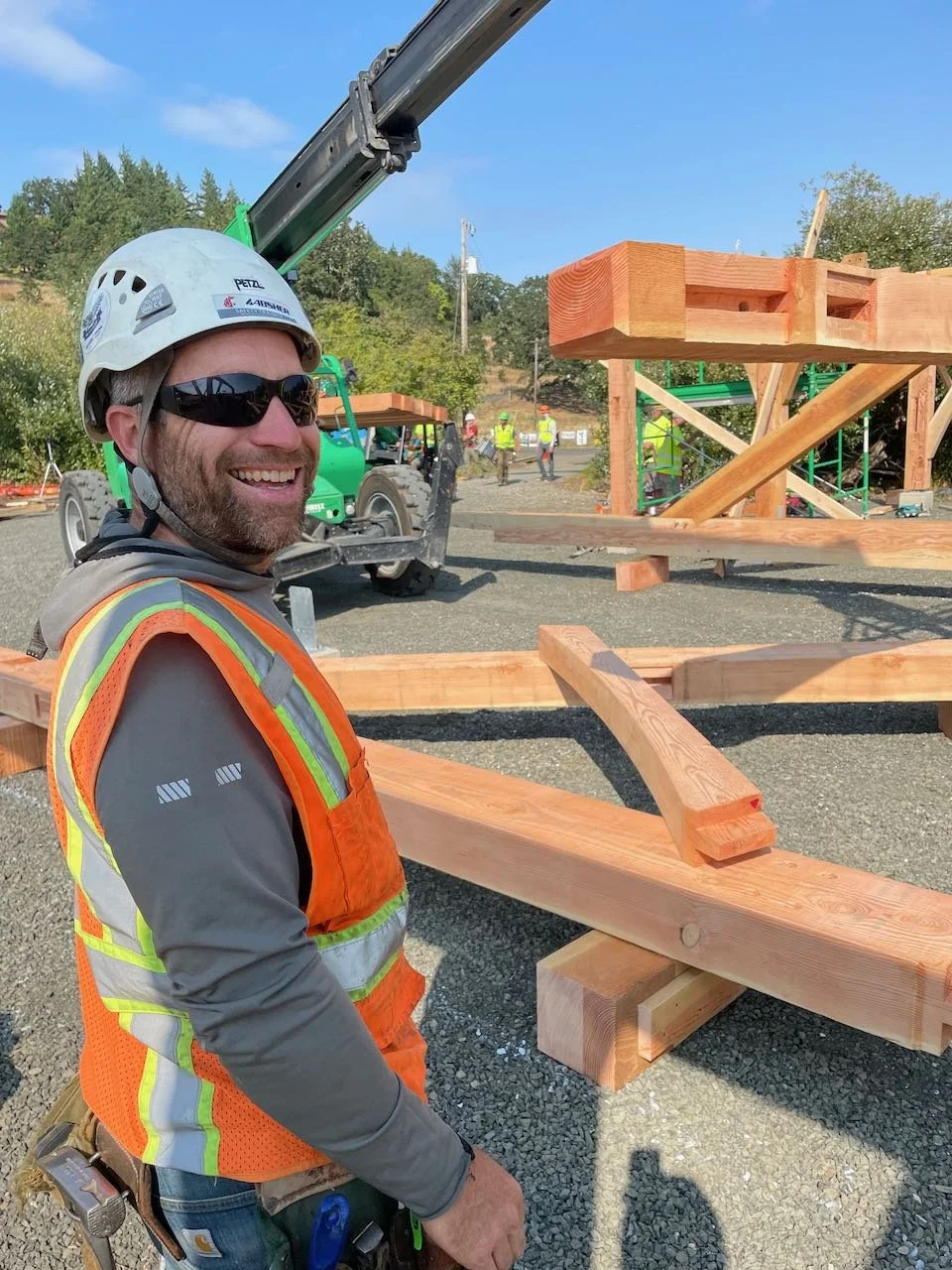 Carpenter in sunglasses smiling and assembling a timber framed truss