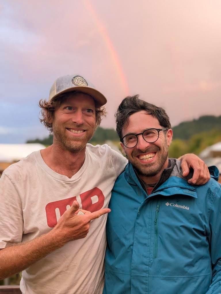 Instructors Ariel Schecter and and David Bowen smiling in front of a rainbow