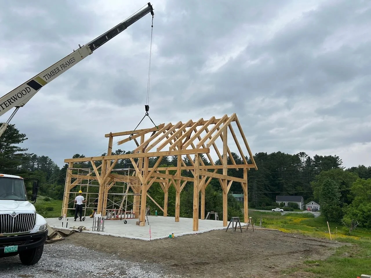 Crane raises rafters near end of timber frame raising