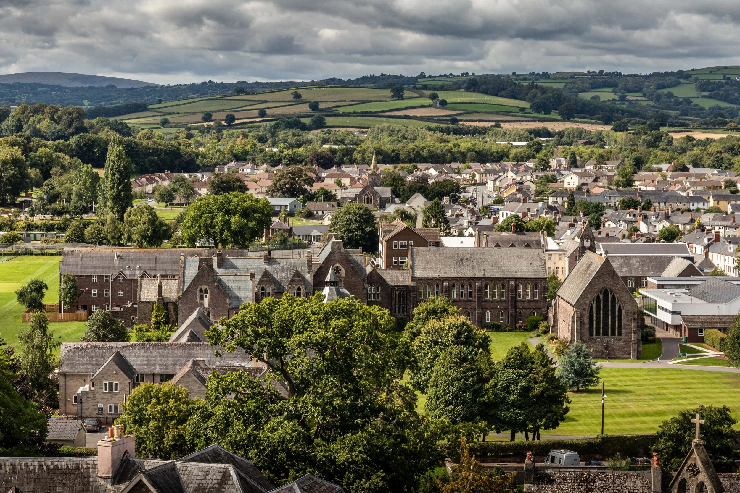 Aerial view of a small town surrounded by green countryside with stone buildings, trees, and fields.
