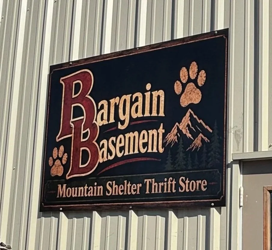 Sign for Bargain Basement, Mountain Shelter Thrift Store, featuring mountain and paw print graphics.