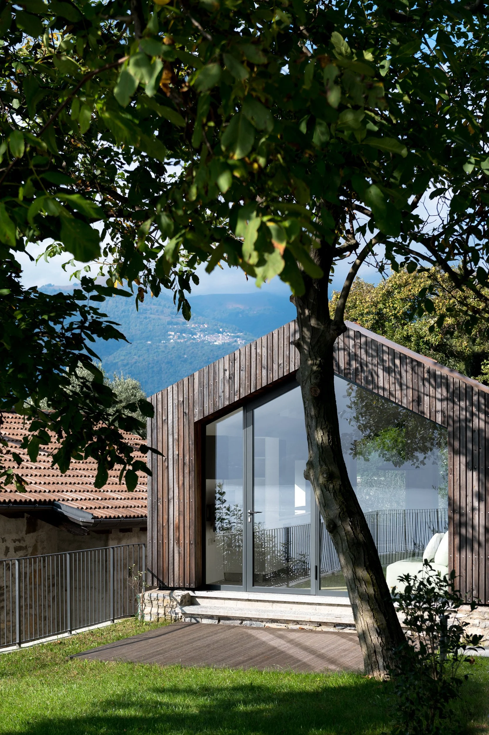 Casa con ampliamento moderno in legno, vetrata ampia e vista sul lago, immersa nel verde.
