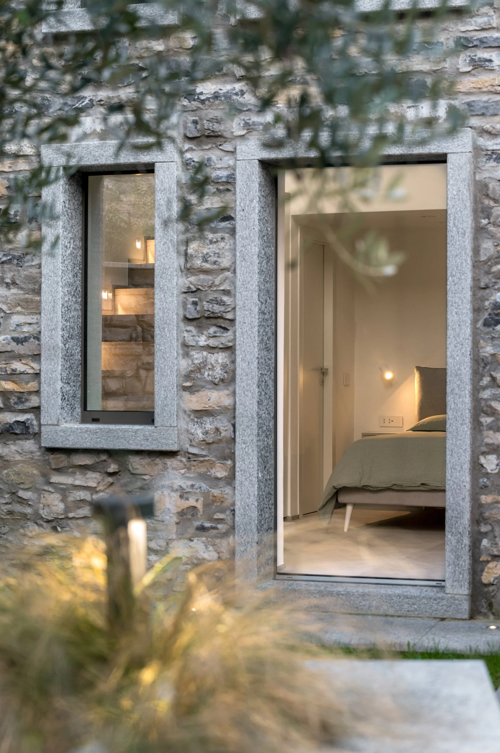 Vista esterna di una camera da letto con luci soffuse, incorniciata da una facciata in pietra.