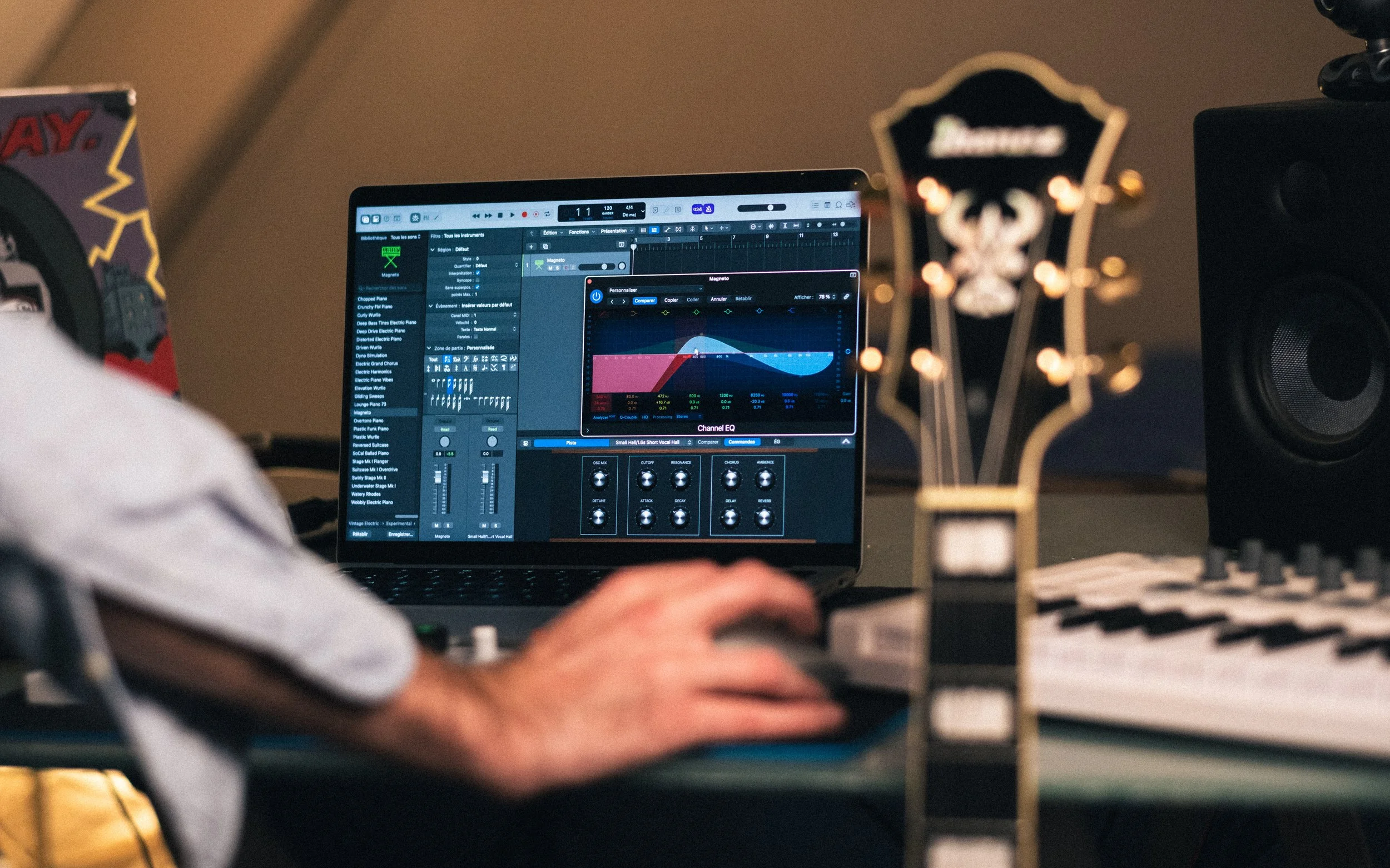 Personne utilisant un ordinateur portable avec un logiciel de production musicale affiché, entouré de matériel audio et musical dans un studio