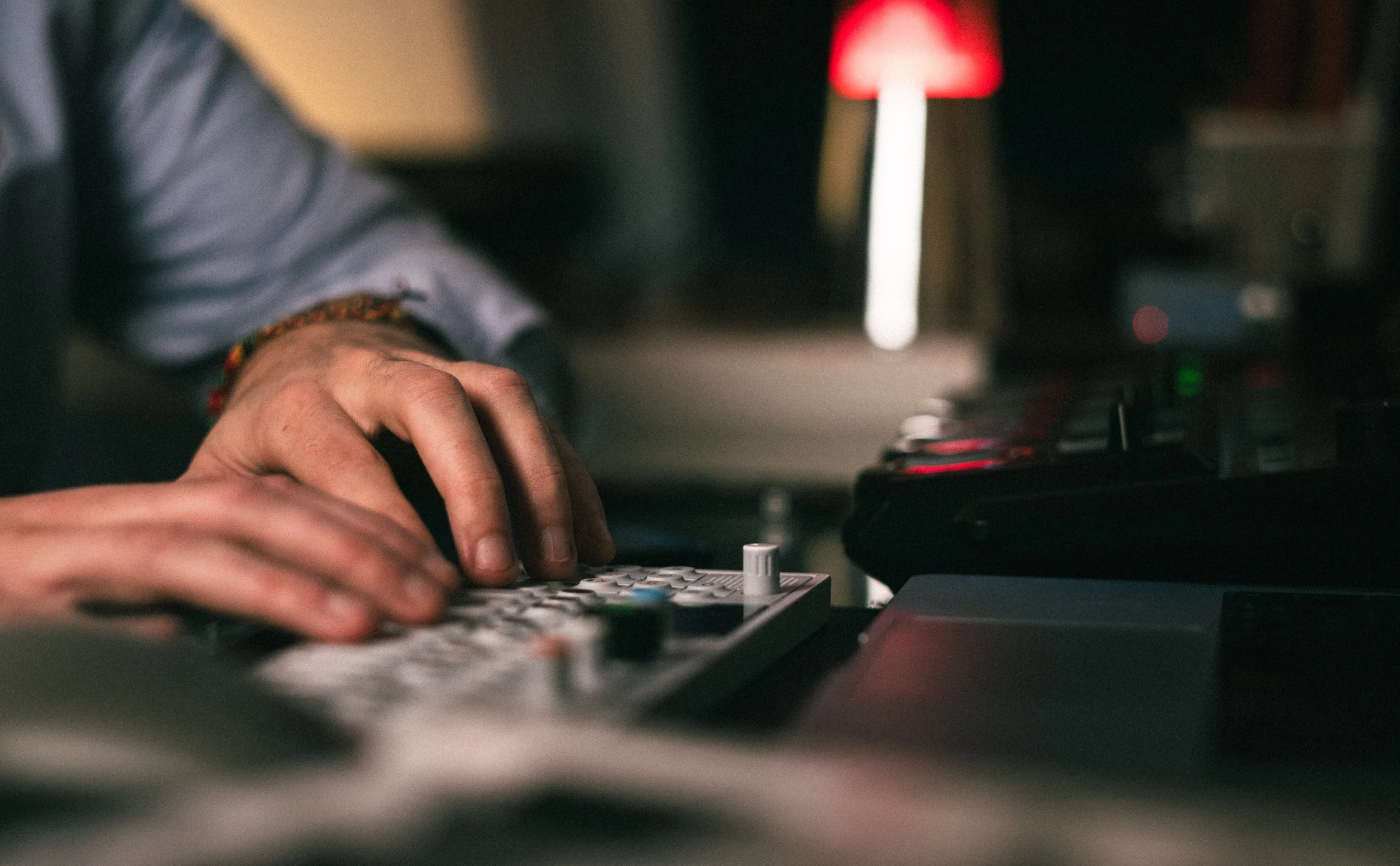 Une personne manipulant un contrôleur de musique ou un kit de production musicale sur un bureau, avec un éclairage tamisé et une lampe rouge en arrière-plan.