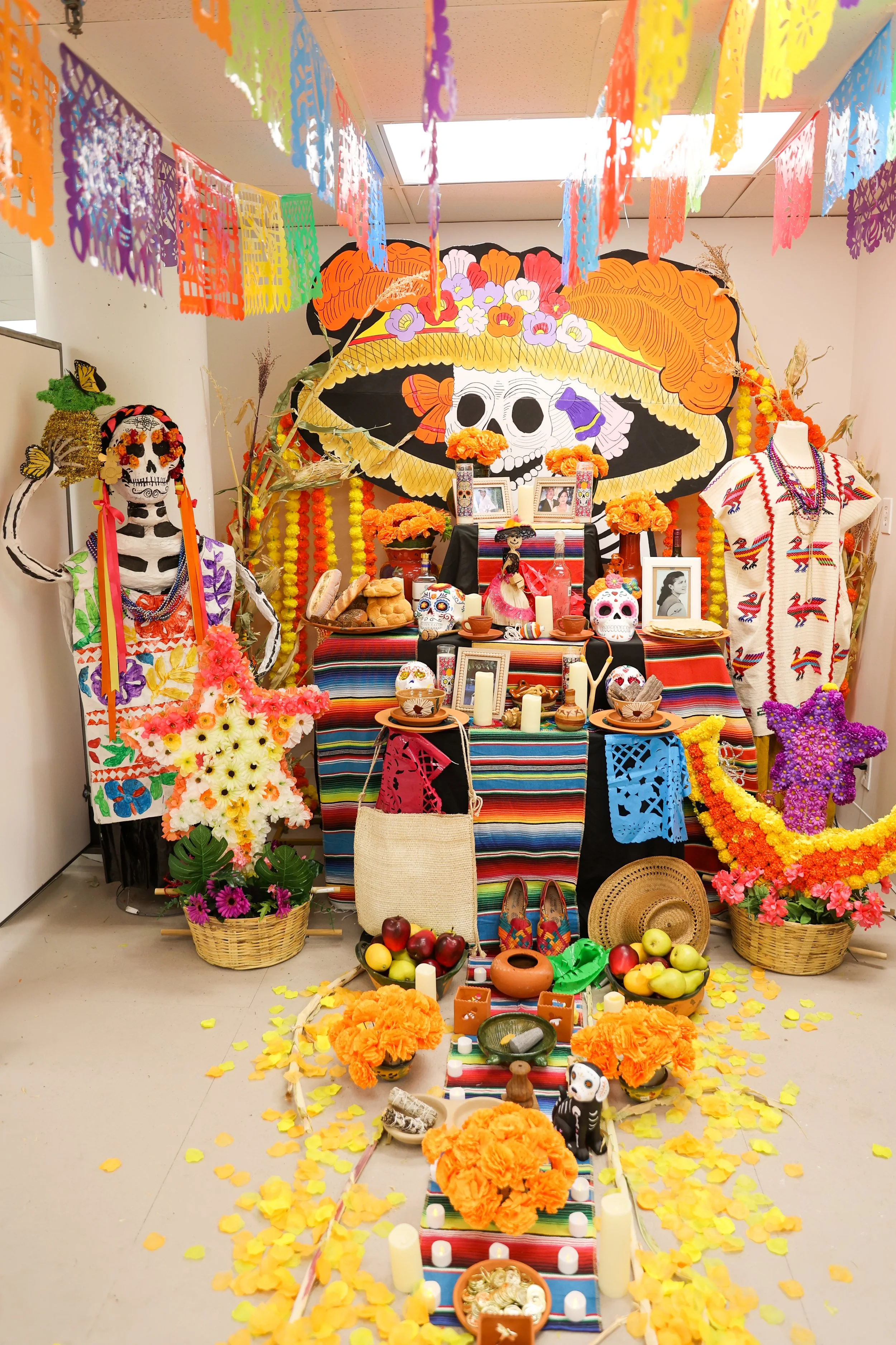 Altar colorido do Dia dos Mortos decorado com flores de calêndula, velas, fotografias, artesanato tradicional mexicano e caveiras de açúcar, com bandeiras de papel picado penduradas acima.