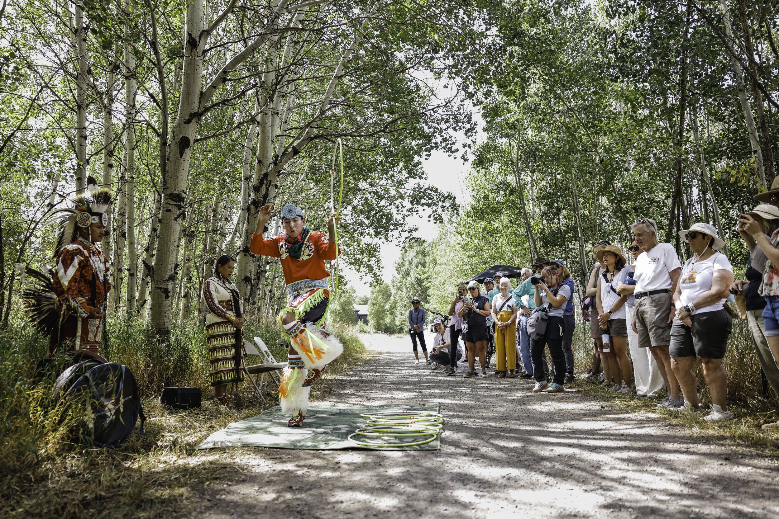 Dançarino nativo americano a apresentar uma dança com arcos numa floresta para um grupo de espectadores.
