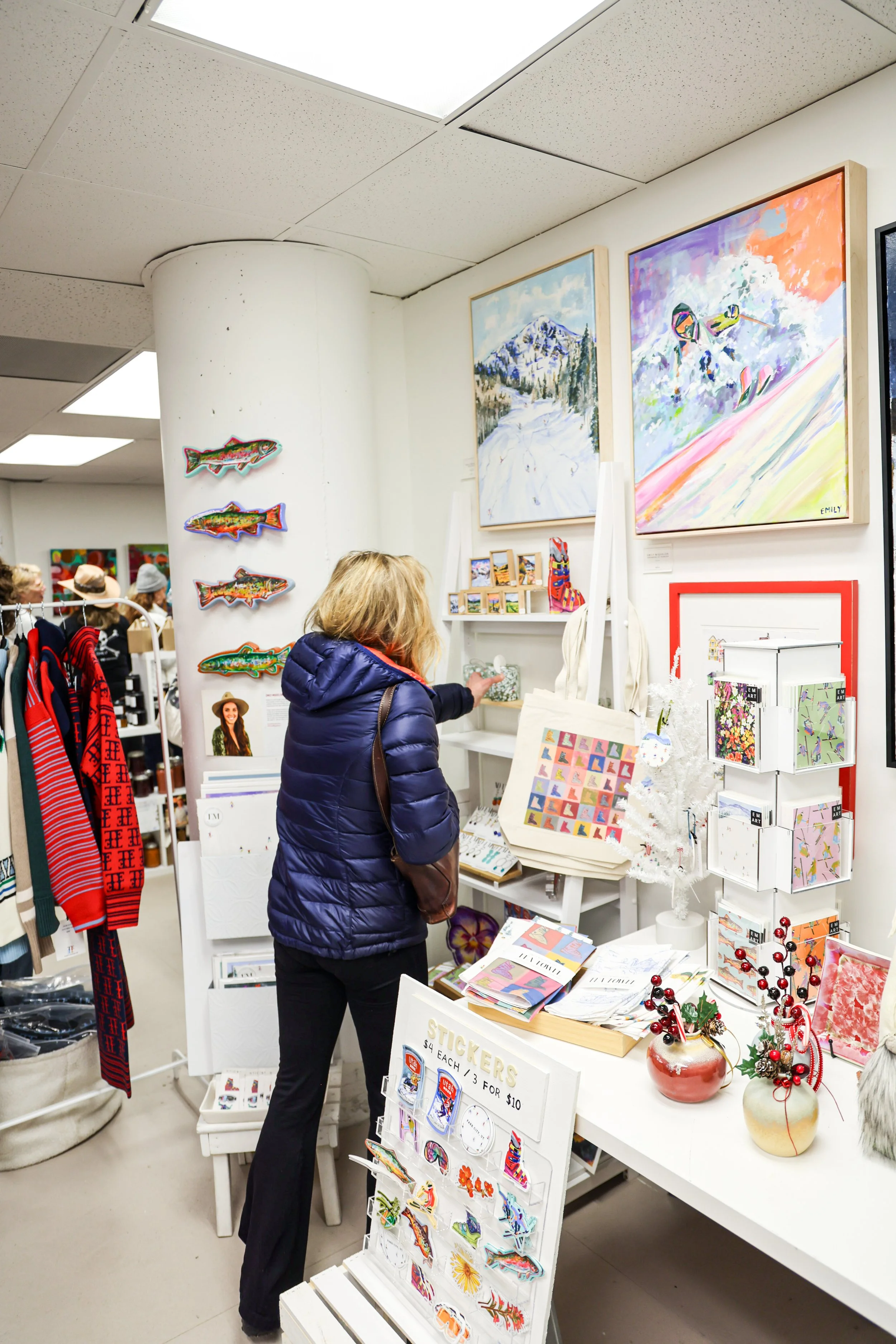 A woman browsing art and gift items in a store, with paintings and decorative objects on display.
