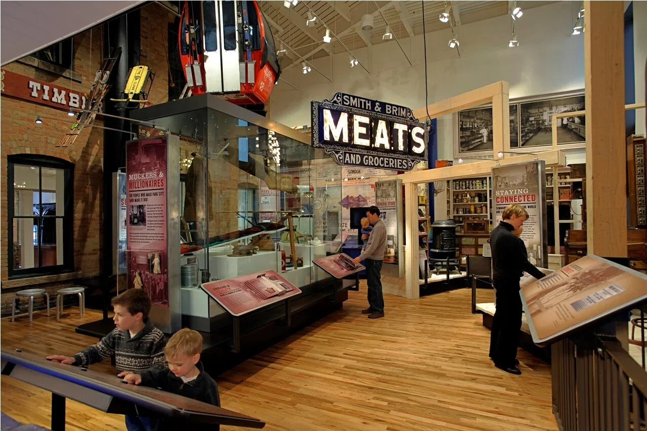 Museum exhibit showing displays of historical items related to meats and groceries, with visitors reading informational panels.
