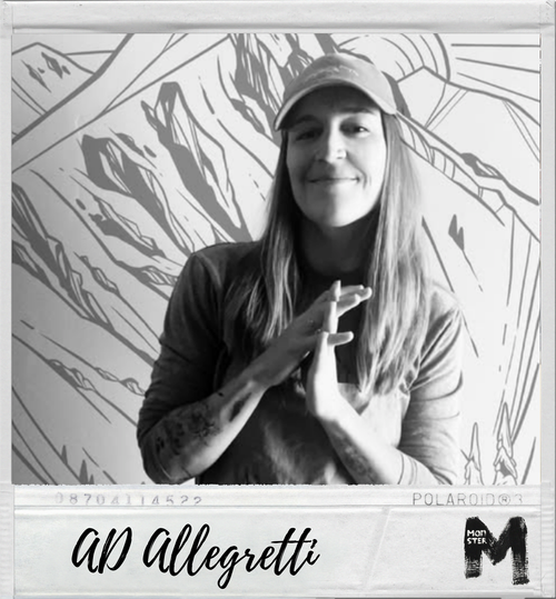 A woman with long hair and a cap smiling and crossing her hands in front of a mural of mountains.