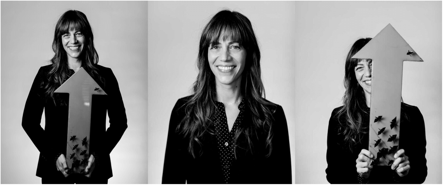 Black-and-white photo of a woman with long wavy hair, smiling, holding an arrow-shaped sign with small decorative elements, in three different poses against a plain background.
