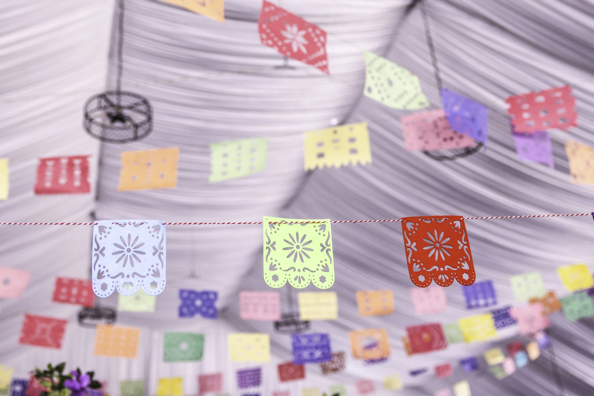 Colorful papel picado banners hanging from a string under a striped canopy at a festive celebration.