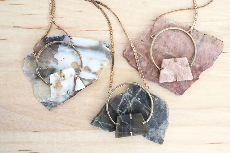 Three necklaces with large, irregularly shaped stone pendants on a light wooden surface.