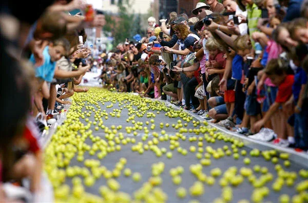 Crowd of people gathered along a path filled with yellow balls, participating in an outdoor event or celebration.