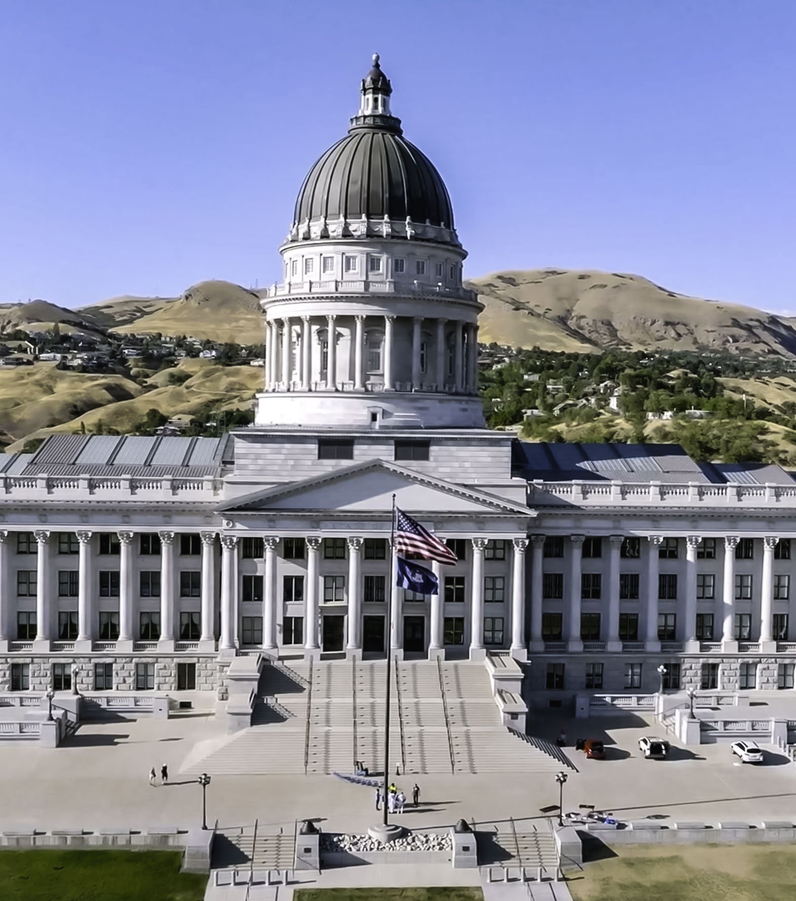 The state capitol building in Salt Lake City, Utah featuring a large dome and columns, with hills and a clear blue sky in the background.