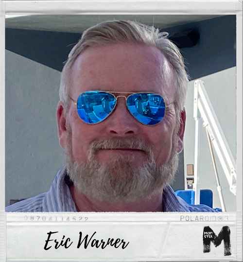 A man with a beard wearing blue mirrored sunglasses smiling for a photo.