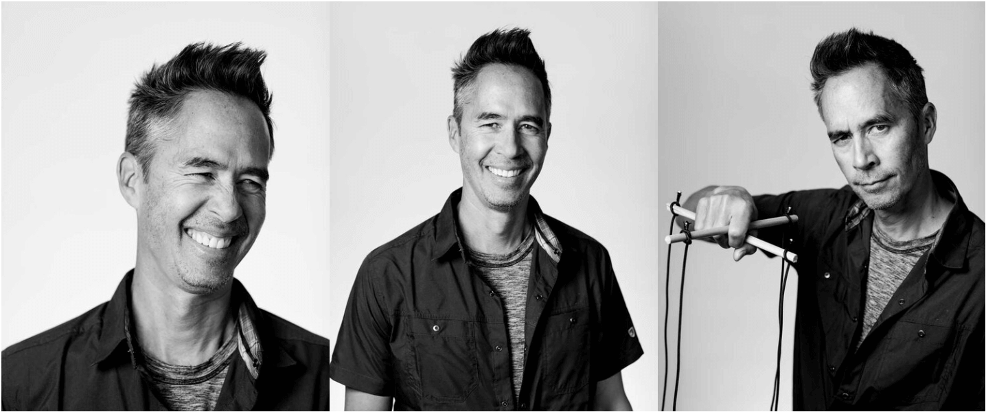 Black and white photo of three men with styled hair and casual clothing. The man on the left is smiling with his eyes closed, the man in the center is smiling with his teeth showing, and the man on the right is holding a slingshot and has a slight smirk.