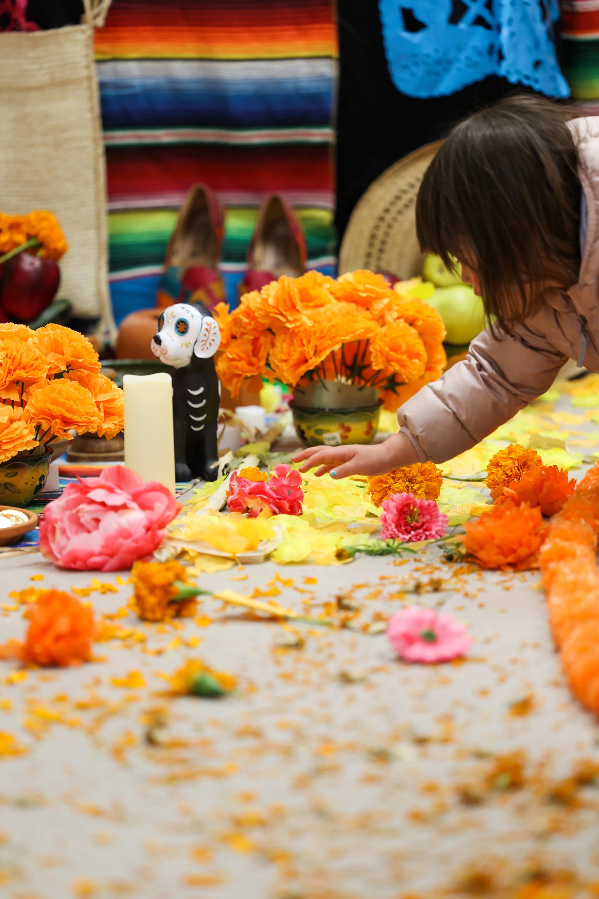 Jovem a arrumar flores coloridas numa mesa decorada para a celebração do Dia dos Mortos, com velas e decorações tradicionais.
