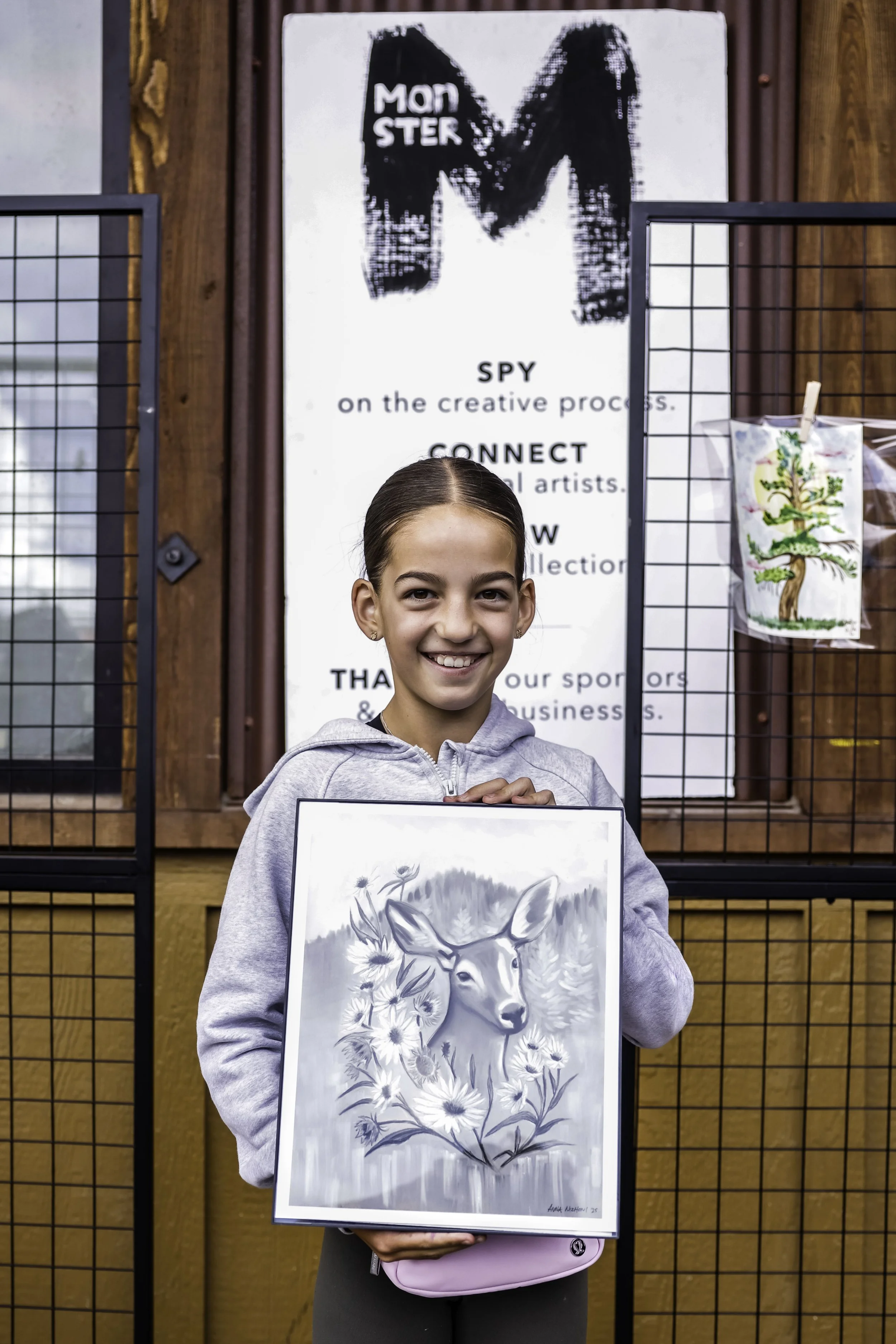 A young girl smiling and holding a framed black-and-white drawing of a deer surrounded by flowers.