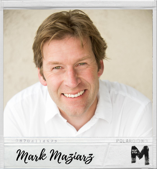 Close-up of a smiling man with light brown hair wearing a white shirt, against a neutral background.