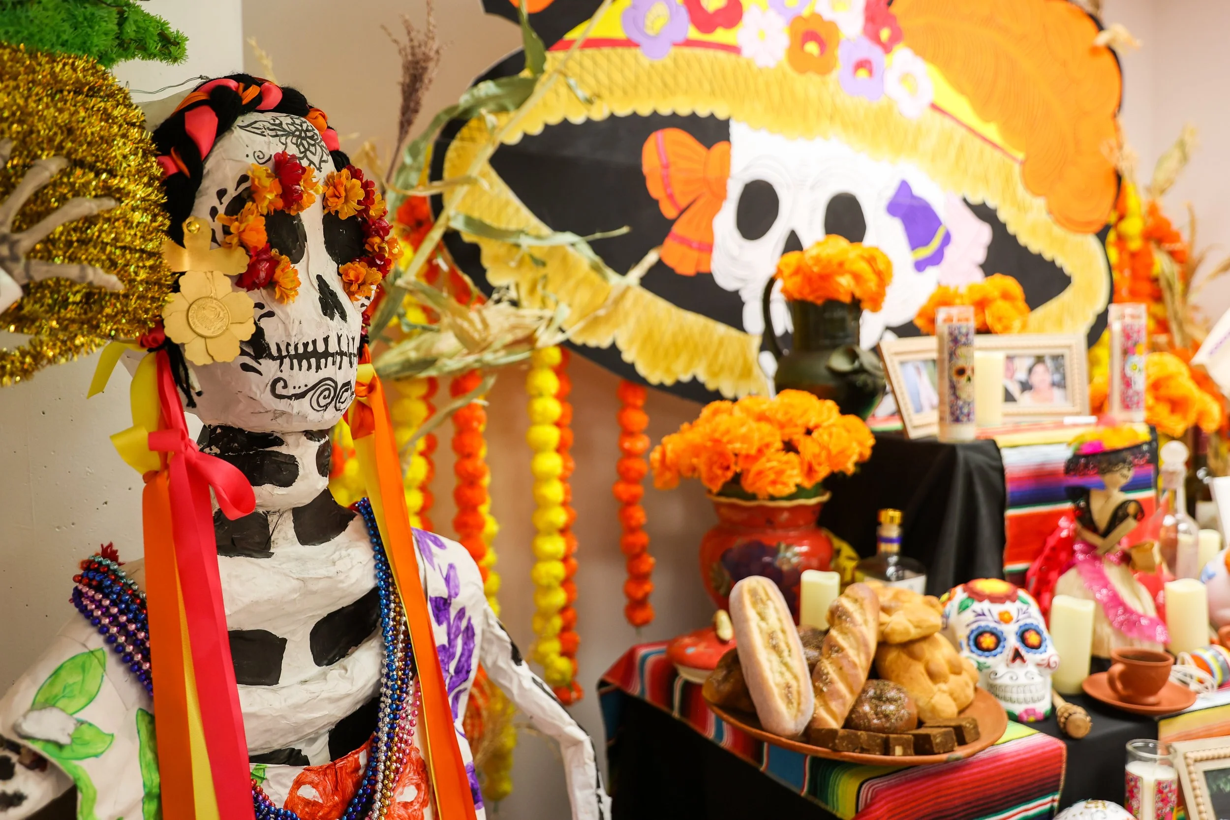Altar colorido do Dia dos Mortos decorado com flores de calêndula, caveiras de açúcar, velas, fotografias emolduradas e decorações tradicionais mexicanas, com uma figura esquelética adornada com miçangas, fitas e flores.