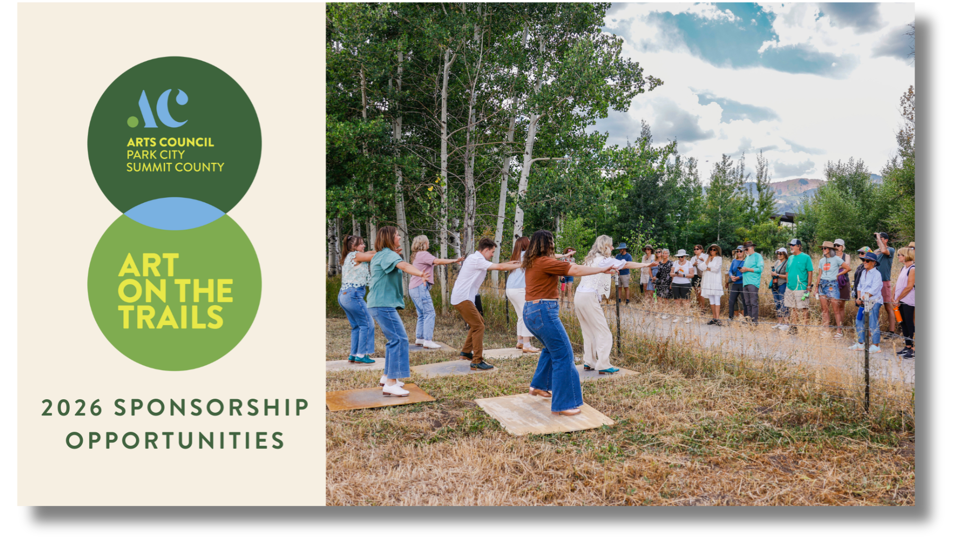 An outdoor event with a group of people participating in a tug-of-war on a trail in a natural setting, with trees and mountains in the background, under partly cloudy skies.