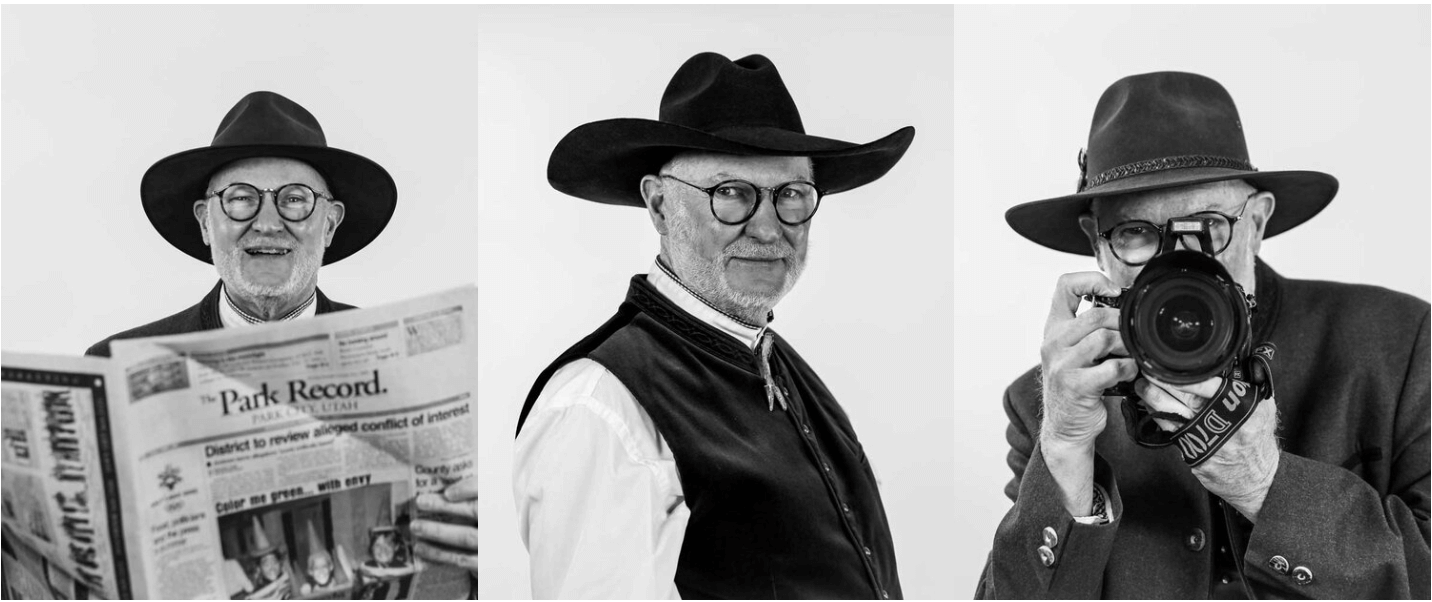 Three older men wearing hats and glasses, posing in front of a plain white background; one is smiling and holding a newspaper, the second is looking sideways with a serious expression, and the third is taking a photo with a camera.