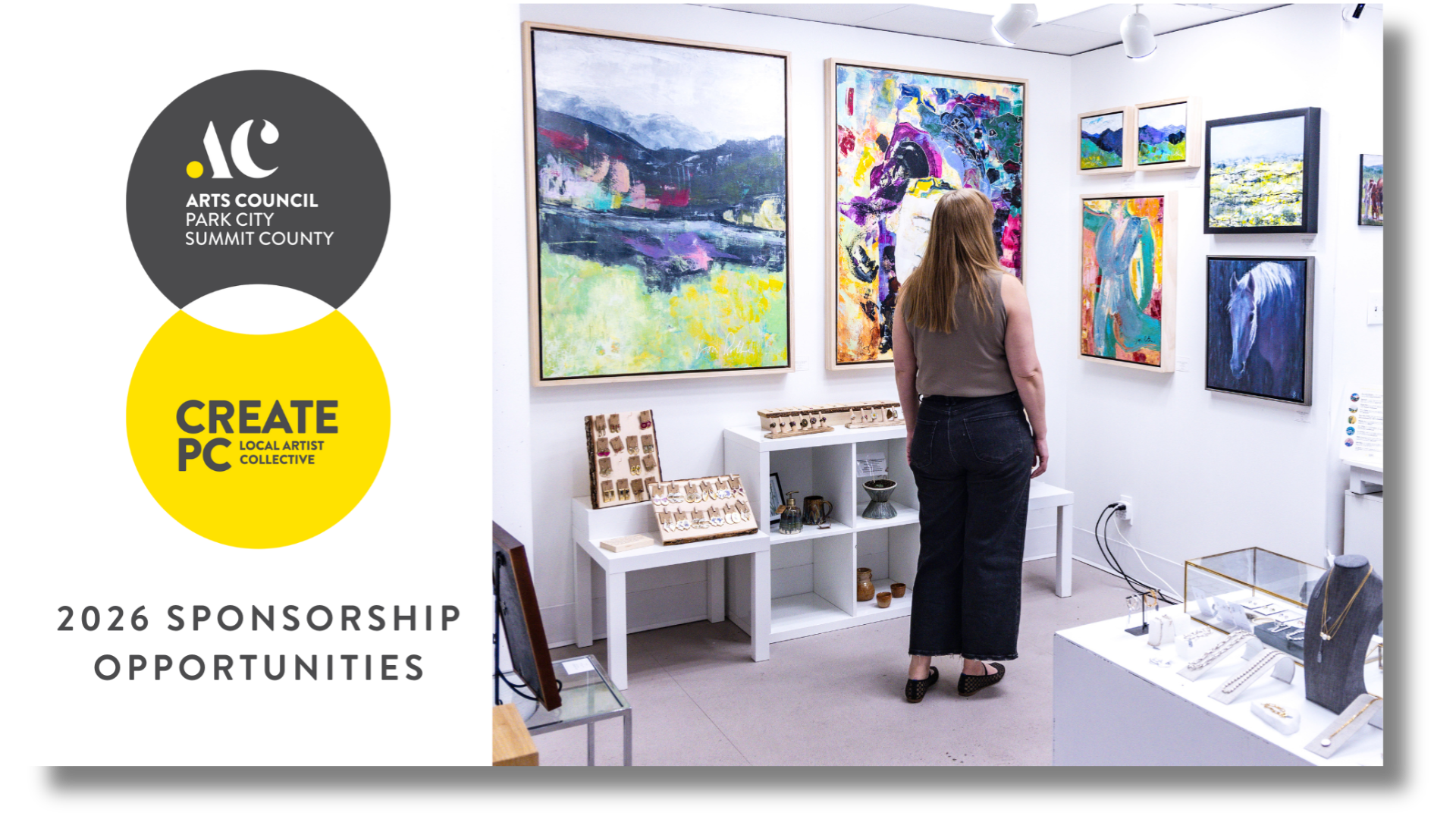 A woman viewing colorful artwork in an art gallery with jewelry displays in the foreground.