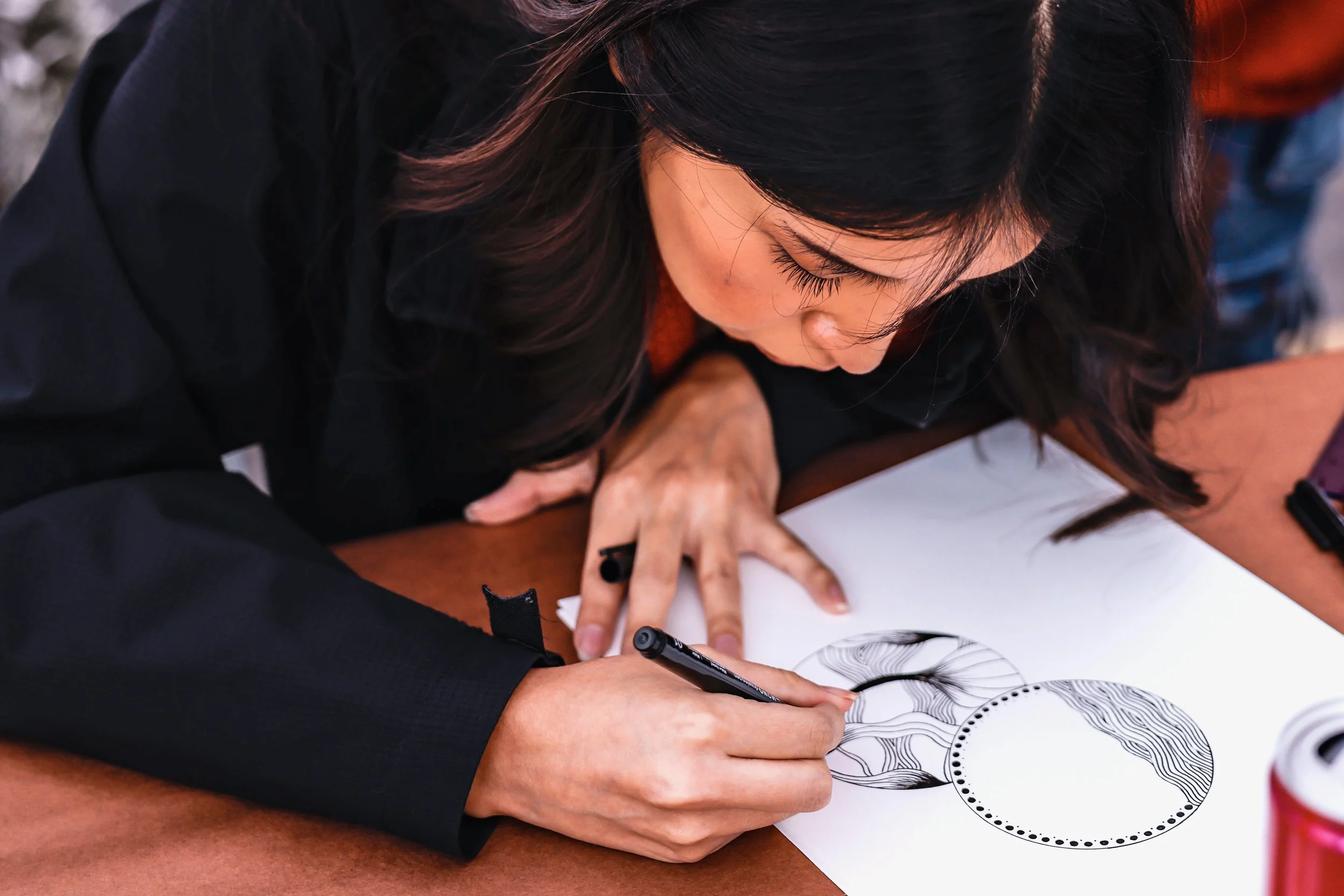 A woman with black hair drawing black and white abstract designs on paper with a marker.