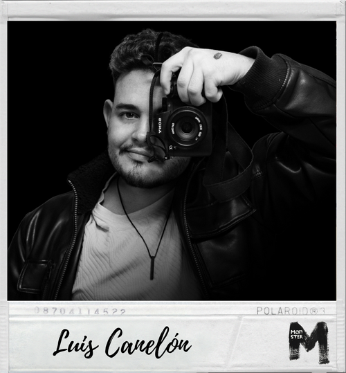 Young man taking a selfie in black and white, holding a camera over his face, with a leather jacket and a light-colored shirt.