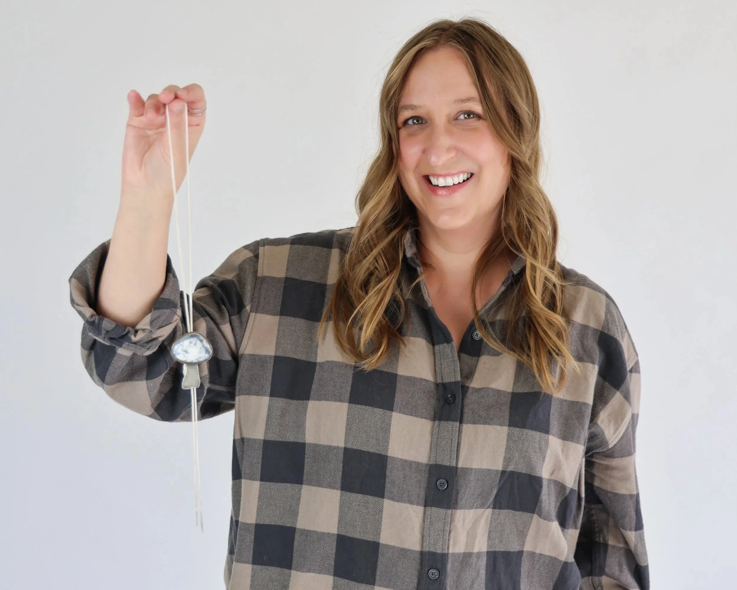 A woman with long, wavy brown hair smiling and holding a bollo tie in her right hand.