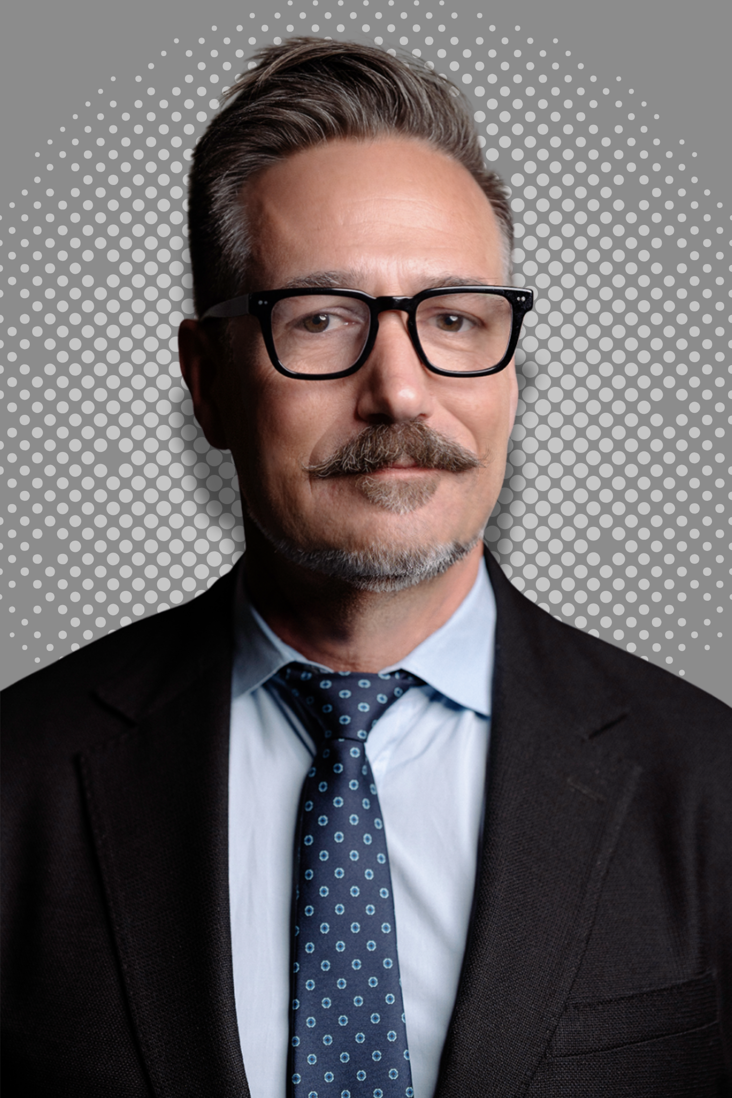 Man wearing glasses, navy suit, and white shirt against a gray dotted background.