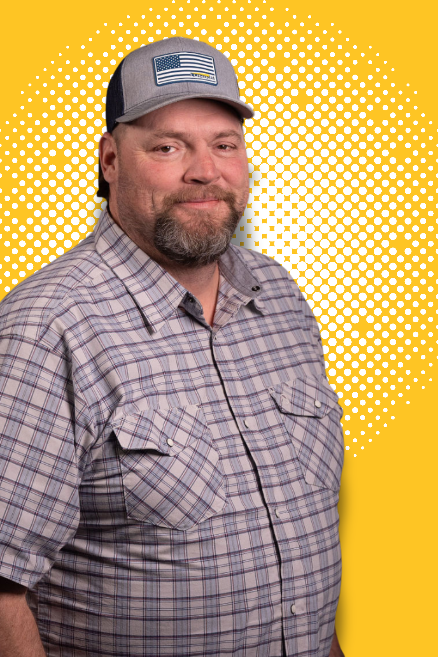 Man wearing a plaid shirt and baseball cap with an American flag design, standing against a yellow dotted background.